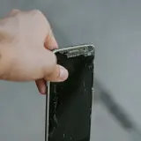 En hand håller en trasig Samsung-mobil. Dags att återvinna mobiltelefonen för att spara på jordens resurser.