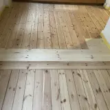 Renovering av ett gammalt trägolv, troligen från 30-talet, med nya plankor som lagts in för att ersätta skadade delar.