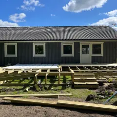 Byggnation av altan med synlig stomme och trapp. Material ligger utspritt, redo för att bli en fin duk under altanen.