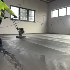 Arbetare polerar nylagd betong med en maskin. Golvet är fortfarande fuktigt och reflekterar ljuset. En del av ballast betong syns längs kanten.