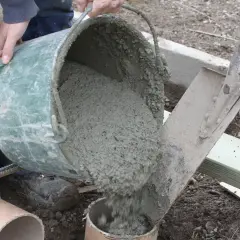 Hink med färdigblandad betong hälls ner i ett rör. En arbetare i blåa arbetskläder ser till att allt går rätt till. Skillnad cement betong är viktig för hållbarheten.