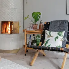 Vacker kakelugn med tänd eld. En stol med pläd och kudde står bredvid ett serveringsbord med drycker. Tänk på renovera kakelugn pris för en mysig atmosfär.