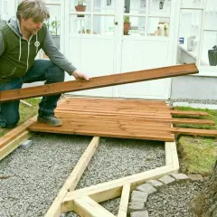 Man lägger trallbrädor för att underhåll altan. Ett nytt trädäck tar form vid växthuset.