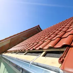 Taktegel i rött läggs på ett hus under uppbyggnad. En kran syns i bakgrunden, redo att lyfta material för framtida byggnadsintegrerade solceller.