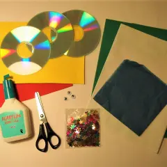 Här är material för att pyssla med gamla CD-skivor: lim, sax, glitterstjärnor, papper i olika färger och två små ögon.