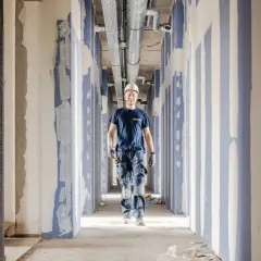 Byggarbetare i en korridor under provtryckning med luft. Rörsystem syns i taket.