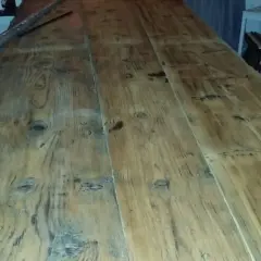 Ett långt, grovt såpskura bord av träplankor. Det ser ut att vara nyligen rengjort och redo för användning.