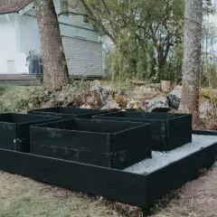 Nya pallkragar i svart trä står redo för plantering. Grus runt pallkragar ger en snygg och praktisk yta.