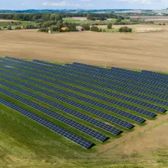 En stor solcellspark på åkermark, med rader av solpaneler som sträcker sig över grönskande och brun jordbruksmark.