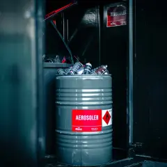 En grå tunna fylld med tomma sprayflaskor, märkt "AEROSOLER", redo för tomma sprayflaskor återvinning.