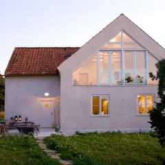 Ett modernt hus med stora fönster och en takkupa, omgivet av grönska. En uteplats med bord och stolar. Detta hus har en bra energideklaration.
