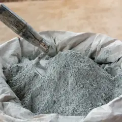 En säck med cement och betong, en murslev vilar i den gråa pulvret, redo för byggprojekt.