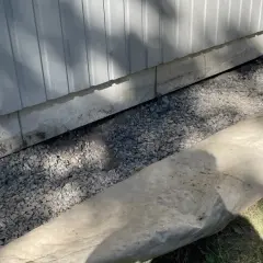 Grå makadam fyller utrymmet under husets grund, en del av arbetet med att bestämma hur mycket makadam under platta som behövs för dränering.