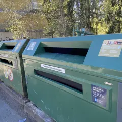 Gröna kärl för pappersåtervinning utomhus. En skylt visar vad som får slängas.