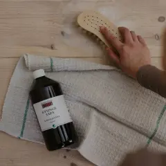 En hand skrubbar trägolv med en borste och linoljesåpa. Flaskan med linoljesåpa är märkbar, men var försiktig, den är brandfarlig.