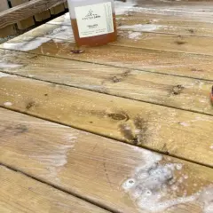 Rapssåpa gör altanen ren och fräsch. En flaska med såpa och en stövel på den skrubbade träaltanen.