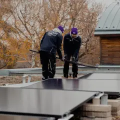 Två personer arbetar med återvinning av solceller på ett tak. Höstfärger syns i bakgrunden.
