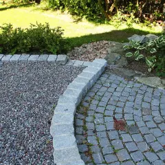 En vacker grusgång entre med stenläggning och kantsten. Gräsmattan och buskar i bakgrunden.
