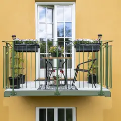 En charmig balkong, byggd på stolpar, med blomlådor, ett litet bord och stolar.