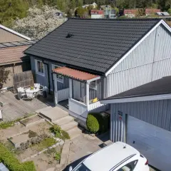 Ett charmigt hus med nummer bbr 21. Trädgårdsmöbler på altanen, en grill och en vit bil framför garaget.