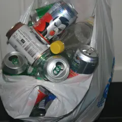 En plastpåse fylld med tomma burkar och flaskor, redo för pant. Här finns bland annat Fanta, ölburkar och en flaska med gul kork.
