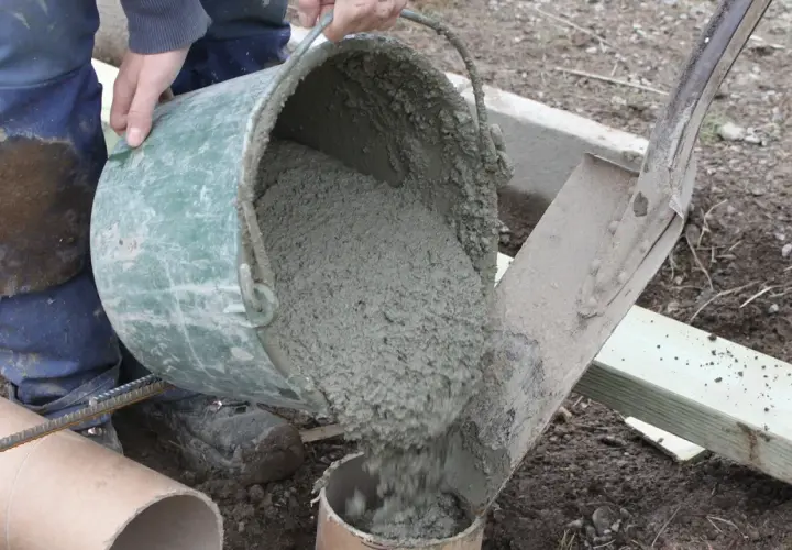 Hink med färdigblandad betong hälls ner i ett rör. En arbetare i blåa arbetskläder ser till att allt går rätt till. Skillnad cement betong är viktig för hållbarheten.