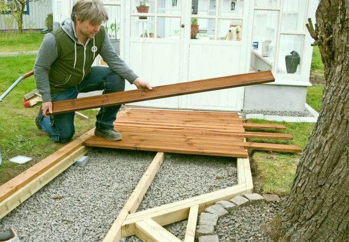 Man lägger trallbrädor för att underhåll altan. Ett nytt trädäck tar form vid växthuset.