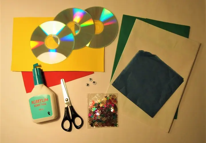 Här är material för att pyssla med gamla CD-skivor: lim, sax, glitterstjärnor, papper i olika färger och två små ögon.