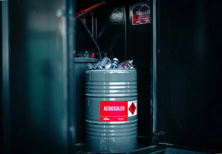En grå tunna fylld med tomma sprayflaskor, märkt "AEROSOLER", redo för tomma sprayflaskor återvinning.