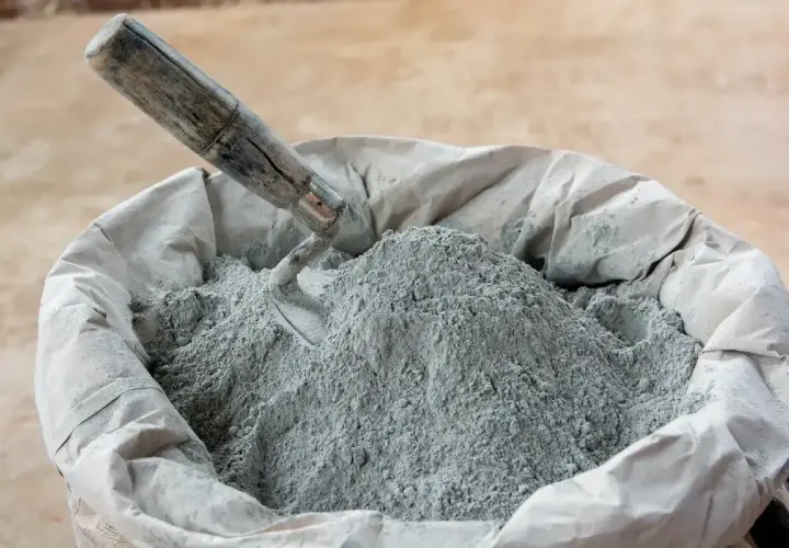 En säck med cement och betong, en murslev vilar i den gråa pulvret, redo för byggprojekt.