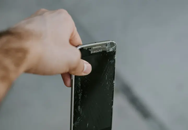 En hand håller en trasig Samsung-mobil. Dags att återvinna mobiltelefonen för att spara på jordens resurser.
