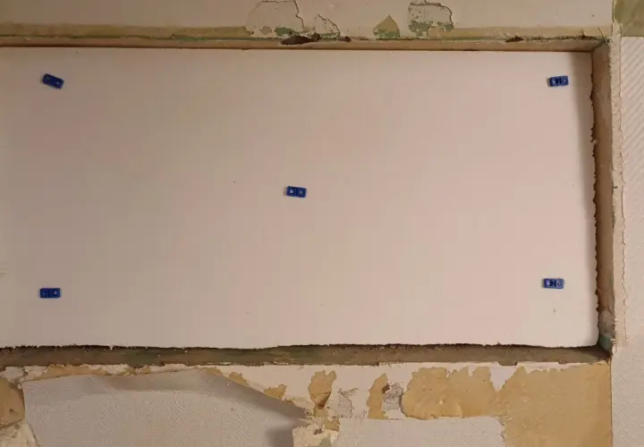 En stor vit cellplastskiva är monterad i en nisch. Blå fästen håller skivan på plats.