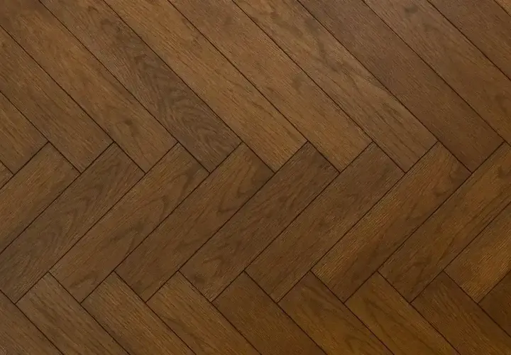 Ett vackert, mörkt gammalt plankgolv lagt i fiskbensmönster.