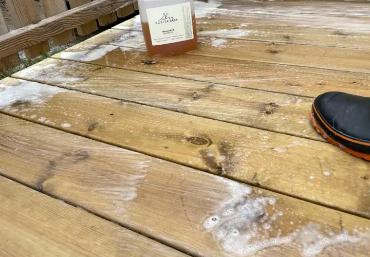 Rapssåpa gör altanen ren och fräsch. En flaska med såpa och en stövel på den skrubbade träaltanen.