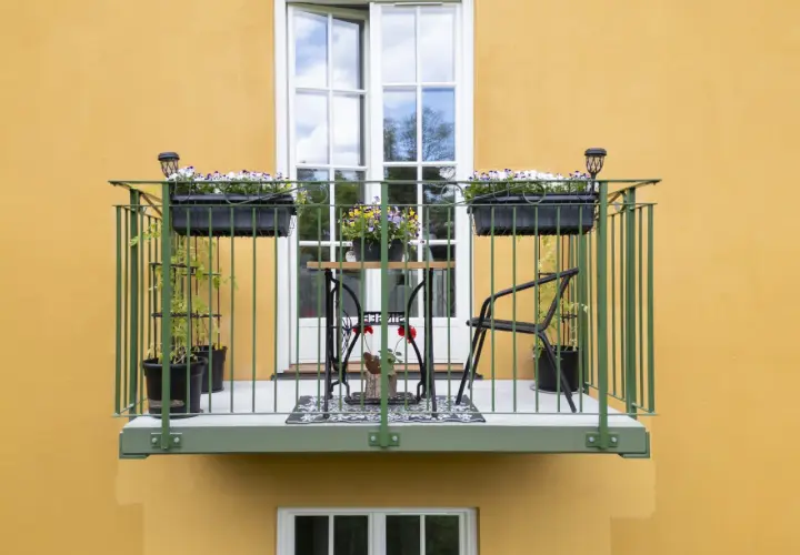 En charmig balkong, byggd på stolpar, med blomlådor, ett litet bord och stolar.