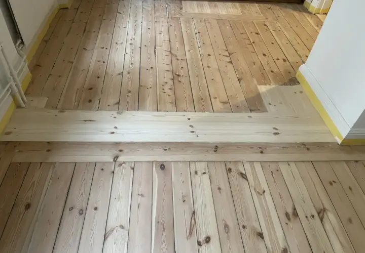 Renovering av ett gammalt trägolv, troligen från 30-talet, med nya plankor som lagts in för att ersätta skadade delar.