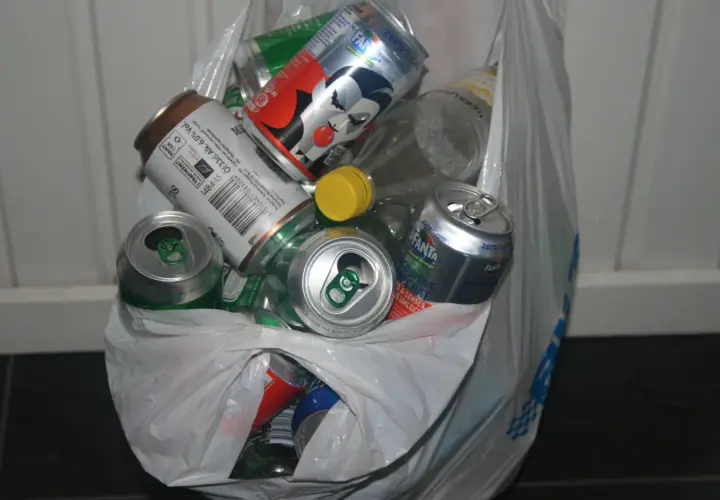 En plastpåse fylld med tomma burkar och flaskor, redo för pant. Här finns bland annat Fanta, ölburkar och en flaska med gul kork.