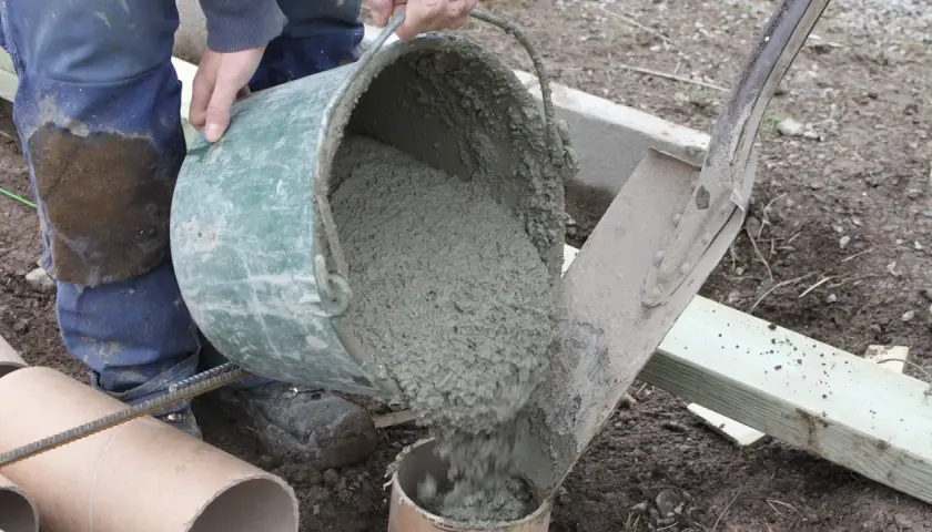 Hink med färdigblandad betong hälls ner i ett rör. En arbetare i blåa arbetskläder ser till att allt går rätt till. Skillnad cement betong är viktig för hållbarheten.