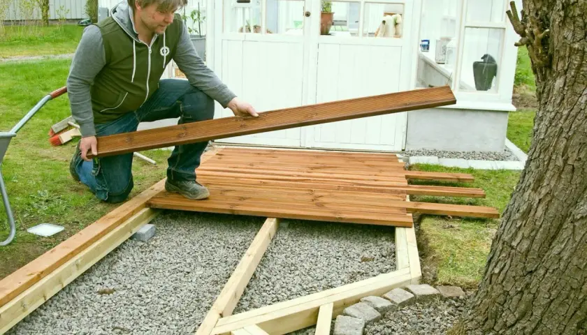 Man lägger trallbrädor för att underhåll altan. Ett nytt trädäck tar form vid växthuset.