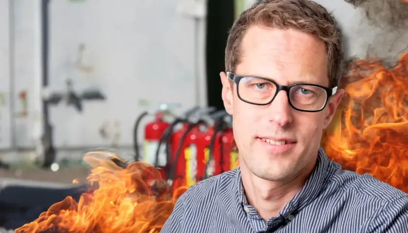 Man med glasögon framför brandsläckare och flammor. En påminnelse om vikten av boverkets byggregler och brandskydd.