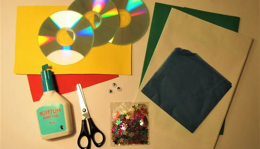 Här är material för att pyssla med gamla CD-skivor: lim, sax, glitterstjärnor, papper i olika färger och två små ögon.