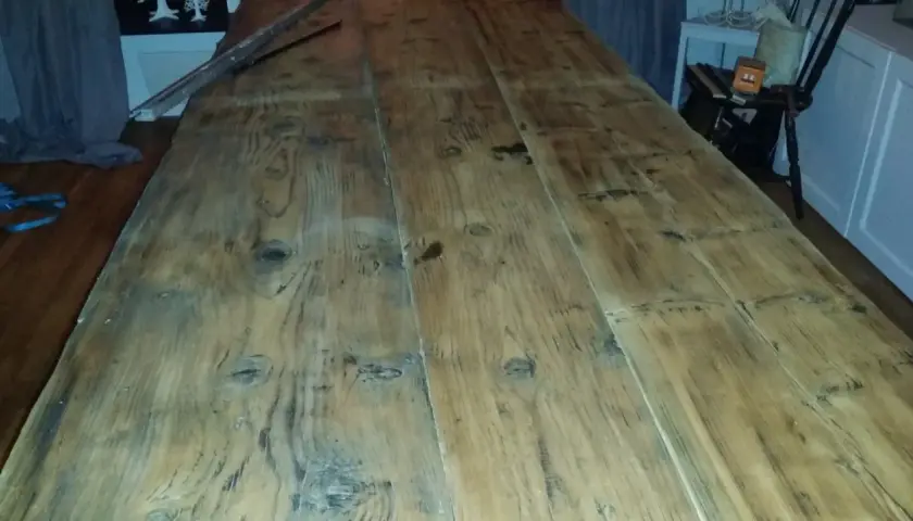 Ett långt, grovt såpskura bord av träplankor. Det ser ut att vara nyligen rengjort och redo för användning.