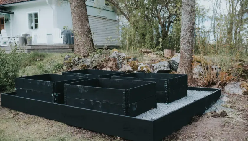 Nya pallkragar i svart trä står redo för plantering. Grus runt pallkragar ger en snygg och praktisk yta.