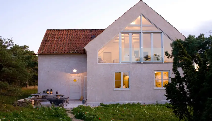 Ett modernt hus med stora fönster och en takkupa, omgivet av grönska. En uteplats med bord och stolar. Detta hus har en bra energideklaration.