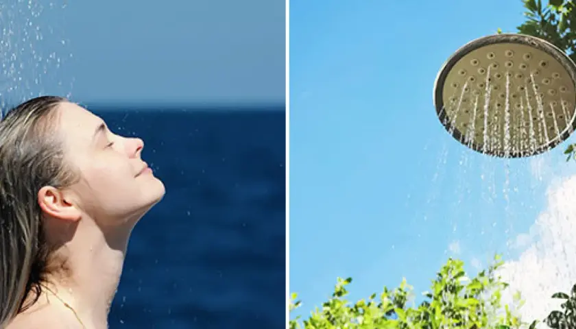 En kvinna njuter av en utedusch med insynsskydd av grönska. Vatten strömmar från en duschmunstycke mot en klarblå himmel.