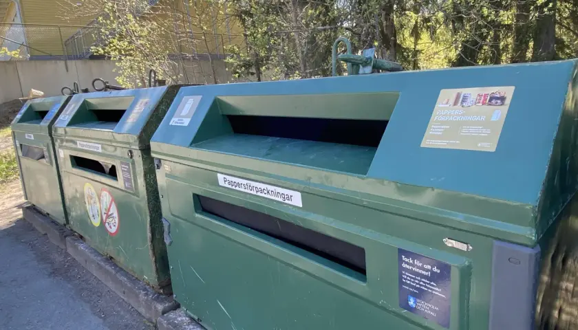 Gröna kärl för pappersåtervinning utomhus. En skylt visar vad som får slängas.