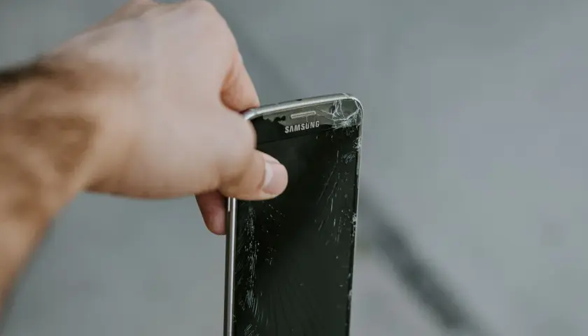 En hand håller en trasig Samsung-mobil. Dags att återvinna mobiltelefonen för att spara på jordens resurser.