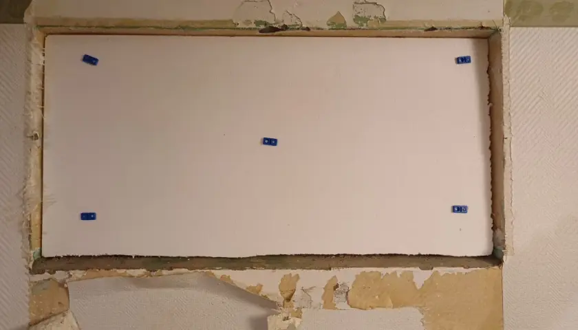 En stor vit cellplastskiva är monterad i en nisch. Blå fästen håller skivan på plats.