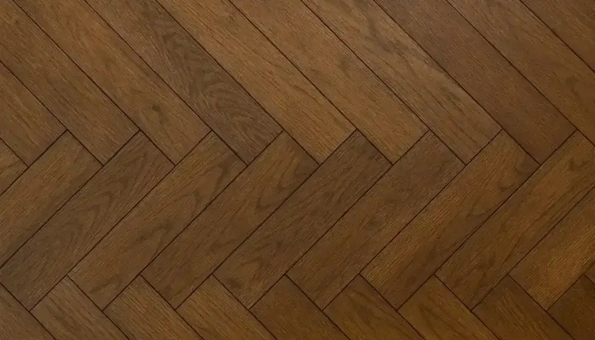 Ett vackert, mörkt gammalt plankgolv lagt i fiskbensmönster.