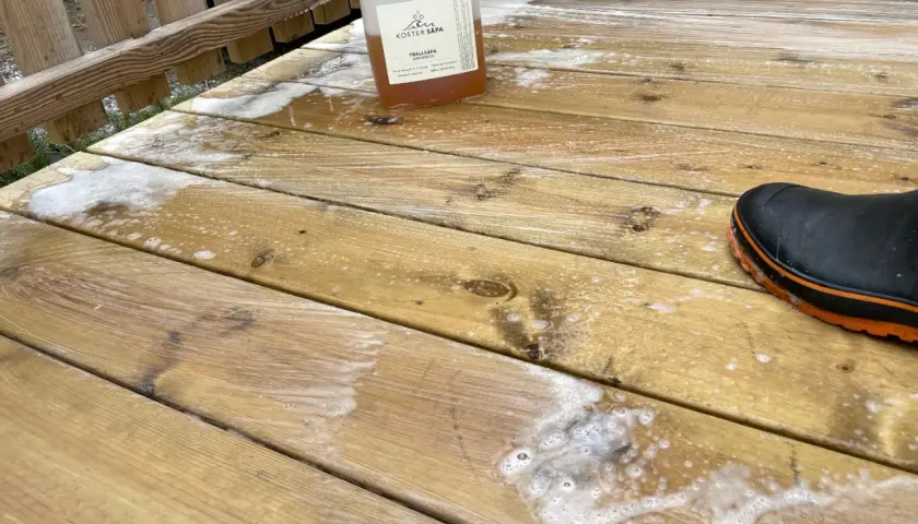 Rapssåpa gör altanen ren och fräsch. En flaska med såpa och en stövel på den skrubbade träaltanen.